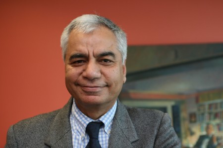 Dinesh Bhugra, Non-Executive Director. Head and shoulder photo of Dinesh standing in front of a red  background
