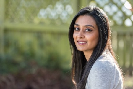 Photograph of a woman outdoors and smiling, turned to look towards the camera
