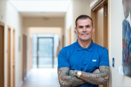 Image of a man looking towards the camera, indoors and smiling with their arms crossed